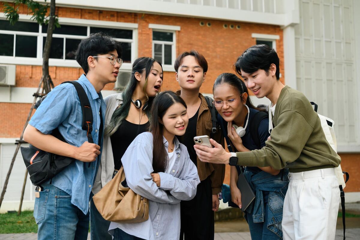Students gathered around one phone screen on a campus lawn